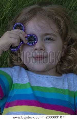 Little child is playing with the spinner lying on the green grass