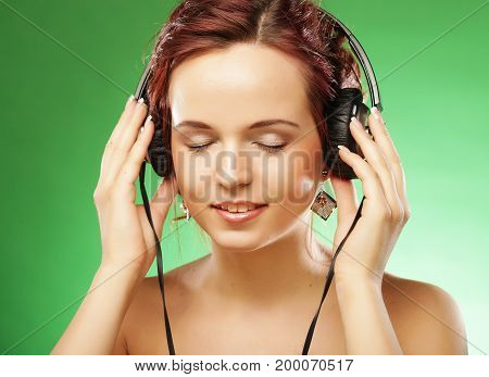 Young happy woman listening to music with headhones. Green background.