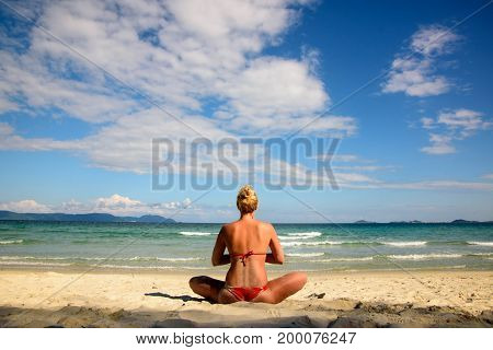 Woman meditating on beach in lotus position. View from the back
