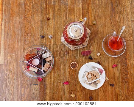 Top view of a composition of traditional breakfast. A plate of powdered cookies, chocolate sweets and biscuits on a wooden table background. A cup of red tea and strawberry spicy tea in a kettle.