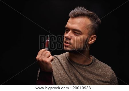 A drug user with a syringe with an injectable drug is in pain on a dark black background, concept, drug addiction, addicted, drugs, equipment for injection.