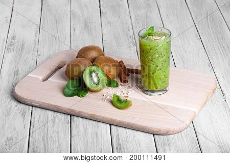 Healthy green cocktail and ingredients on a cutting board and on a gray wooden background. A heap of kiwi and cinnamon sticks on a table. Organic, natural and detox food. Copy space.