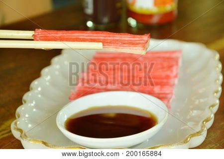 imitation crab stick made from fish dipping with soy sauce on chopsticks