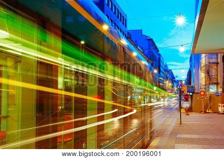 Helsinki, Finland. Tram Departs From A Stop On Street Aleksanterinkatu In Helsinki. Night View Of Aleksanterinkatu Street In Kluuvi District In Evening Or Night Illumination.