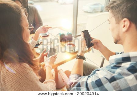 Modern igen. Positive international students using smart phones and sitting in the cafe while enjoying rest together