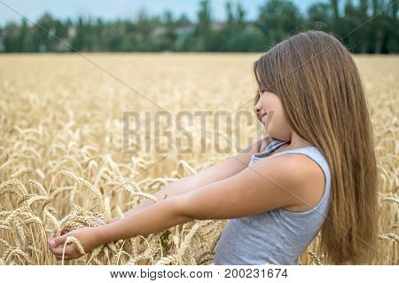 Portrait of adorable little girl with beautiful long hair touching wheat ears in the field on a summer day