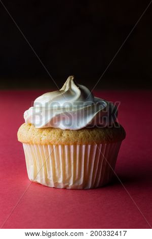 Single lemon custard centred eggwhite meringue decorated sponge cupcake closeup isolated on vertical red background - space for your text