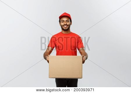 Delivery Concept - Portrait of Happy African American delivery man in red cloth holding a box package. Isolated on Grey studio Background. Copy Space.