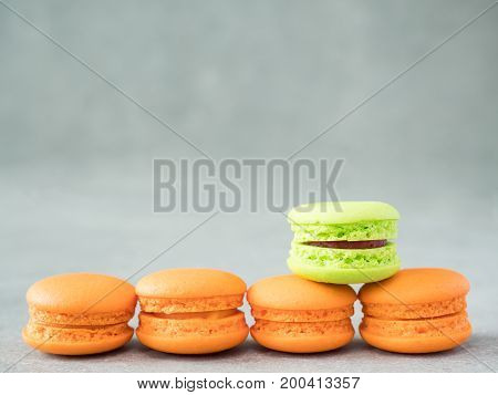 Green color macaroon stand over assortment of orange color macaroon with copy space on bare cement or concrete wall background