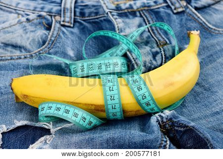Health and male sexuality concept. Jeans zipper and pocket close up. Mens denim pants crotch with banana imitating male genitals. Banana wrapped with blue measure tape on jeans selective focus.