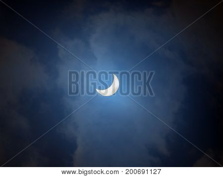 2017 solar eclipse as seen in Glendale Arizona. The sun is partially blocked by the moon and seen through a cloudy sky. If you zoom in you can see two sun spots on the bottom crescent of the sun.