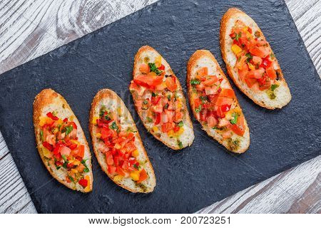 Appetizer bruschetta with chopped vegetables on ciabatta bread on stone slate background close up. Delicious snacks sandwiches crostini canape antipasti on party or picnic time. Top view