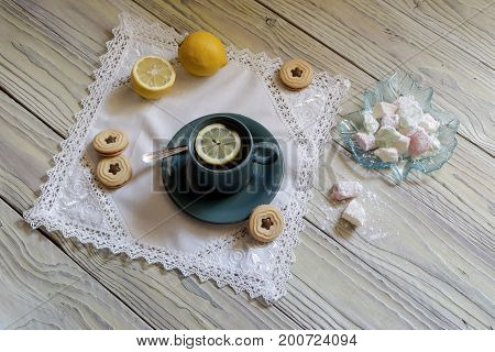 Green cup of tea, lemons, cookies and shark-lukum on a wooden table close-up