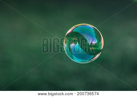 Close up of flying soap bubble with great reflections. Flying over green background