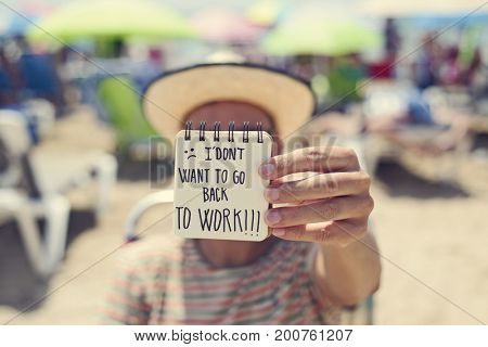 closeup of a young man in the beach showing a spiral notepad with the text I dont want to go back to work handwritten in it
