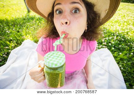 Funny woman drinking green detox smoothie on picnic. Face close up portrait outdoor