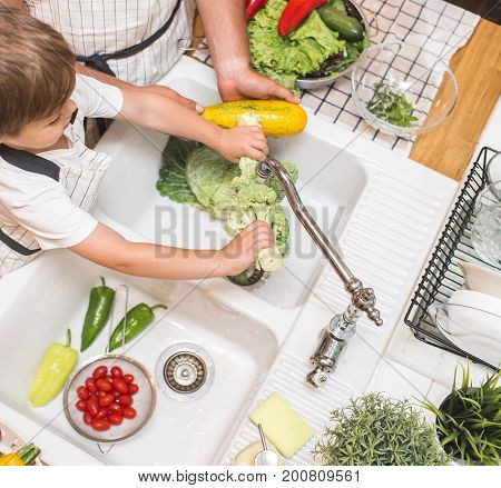 Father with little son washes vegetables on the kitchen before eating