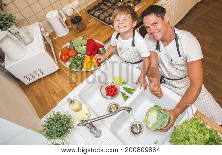 Father with little son washes vegetables on the kitchen before eating