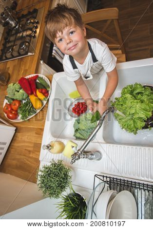 Little boy washes vegetables on the kitchen before eating