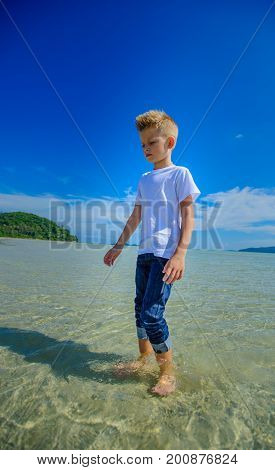 Adorable Boy Having Fun On The Tropical Beach. White T-shirt, Dark Trousers And Sunglasses. Barefoot