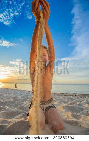 Handsome Eight Years Boy On Beach Performs Acrobatic Sketches And Plays With A Stream Of Sand