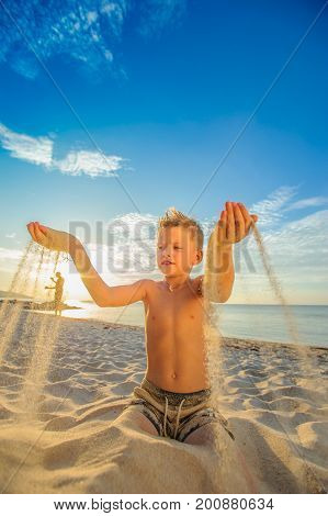 Handsome Eight Years Boy On Beach Performs Acrobatic Sketches And Plays With A Stream Of Sand