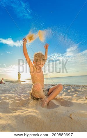 Handsome Eight Years Boy On Beach Performs Acrobatic Sketches And Plays With A Stream Of Sand