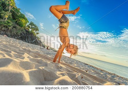 Handsome Eight Years Boy On Beach Performs Acrobatic Sketches And Plays With A Stream Of Sand