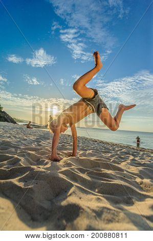 Handsome Eight Years Boy On Beach Performs Acrobatic Sketches And Plays With A Stream Of Sand