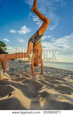 Handsome Eight Years Boy On Beach Performs Acrobatic Sketches And Plays With A Stream Of Sand