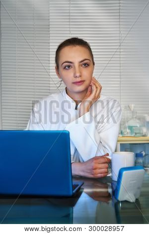 Young Medtech, Doctor Or Practitioner Drinks Coffee In Front Of Working Laptop In Her Office.
