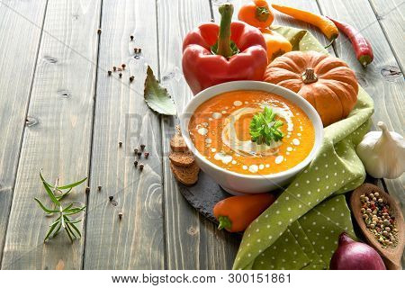 Spicy Pumpkin Soup With Baked Bell Peppers, Chili, Red Onion And Garlic In Ceramic Bowl On The Woode