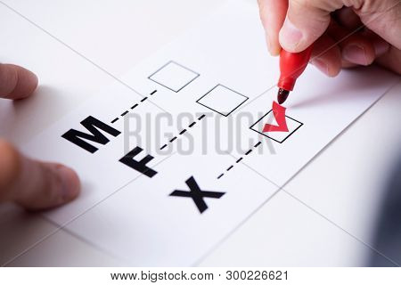 closeup of a young caucasian person marking the X in a form with the letters M for male, F for female and X for the third gender category