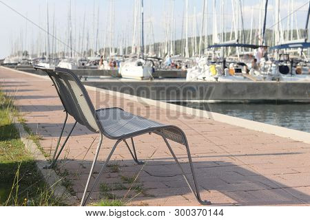 Empty Bench On The Pier Against A Mourings Yachts. Symbols Of Return And Waiting. The Infrastructure