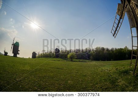 Wooden Windmills In The Middle Of The Field Against The Background Of The Lem And The Sky With The S