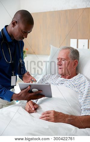 Doctor With Digital Tablet Visiting And Talking With Senior Male Patient In Hospital Bed