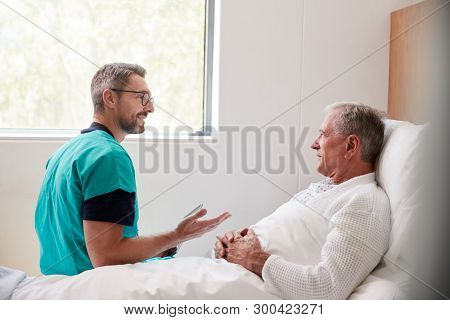 Surgeon Visiting And Talking With Senior Male Patient In Hospital Bed In Geriatric Unit