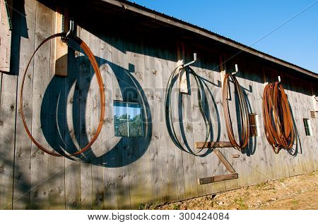Old And Used Bandsaw Blades Throw Their Shadows While Hanging On An Old Weathered Wall Of A Sawmill.