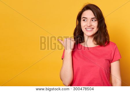 Close Up Portrait Of Young Good Looking Gark Haired Female In Casual Outfit Pointing Left With Thumb