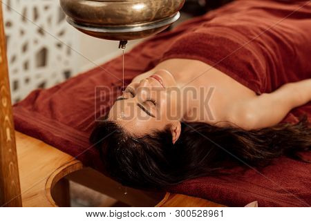 Relaxed Young Woman Lying Under Shirodhara Vessel During Ayurvedic Procedure