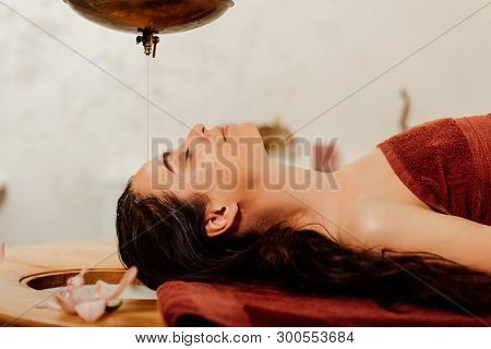 Side View Of Relaxed Young Woman Lying Under Shirodhara Vessel During Ayurvedic Procedure