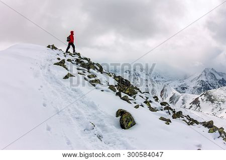 Backpacker Man High In Snowy Mountains. Portrait In A Red Jacket