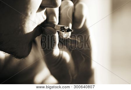 A Black And White Image Of A Man With A Stubble On His Face Smoking A Smoking Cigarette, Holding It 