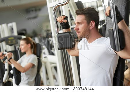 Young Handsome Man Training At Gym. Fit Young Man Is Doing Chest Workout On The Machine In Gym. Perf