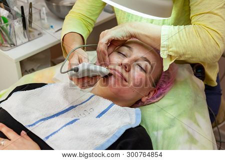 A Young Girl Is Lying On Couch With A Pink Hat On Her Hair While Performing An Ultrasonic Face Clean