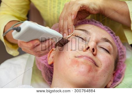 A Young Girl Is Lying On Couch With A Pink Hat On Her Hair While Performing An Ultrasonic Face Clean