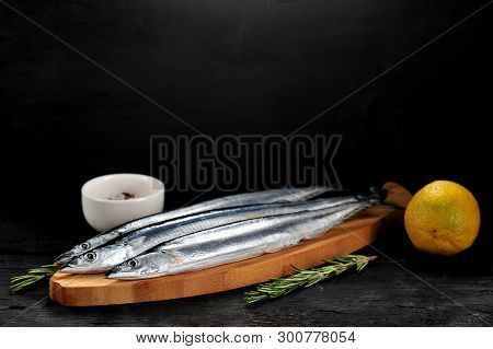 Raw Saury On A Wooden Board In The Form Of Fish With Rosemary And Lemon