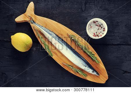 Raw Saury On A Wooden Board In The Form Of Fish With Rosemary And Lemon-top View