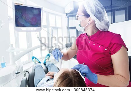A Professional Dentist Woman In Glasses And Overalls Examines The Oral Cavity Of A Young Girl In The