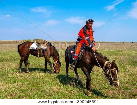 DECABRIST VILLAGE, SARATOV REGION, RUSSIA - APRIL 28, 2019: A shepherd man rider riding a black horse in a field
